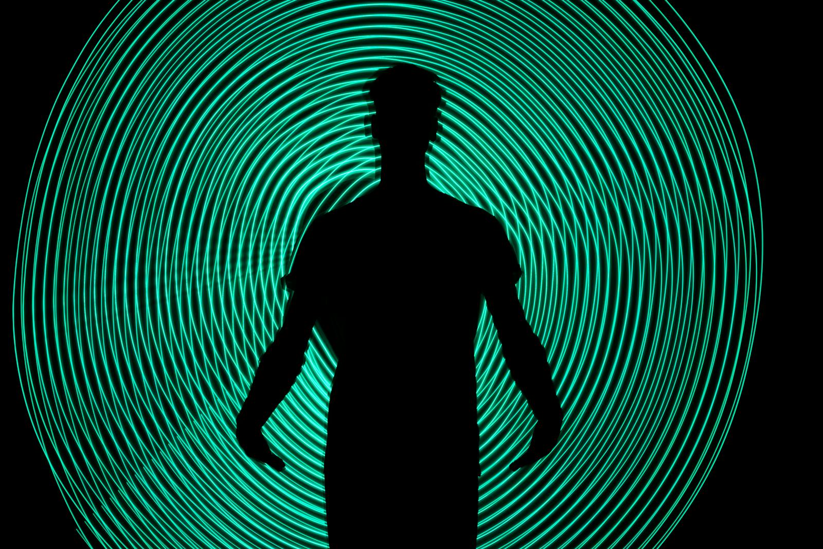 Silhouette of a man standing against dynamic green light swirls. Captivating and abstract art.